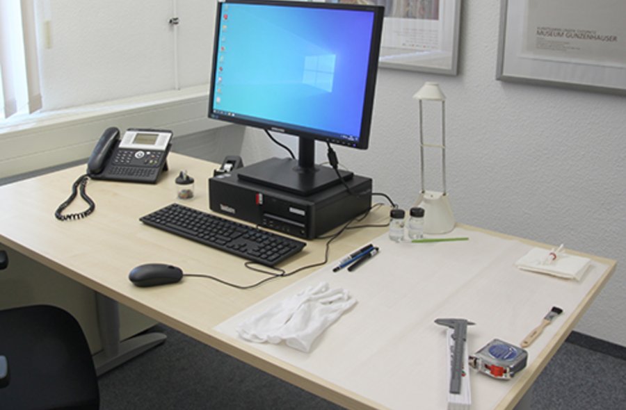 Foto eines Schreibtisches, auf dem prominent ein Computerbildschirm und eine Tastatur platziert sind