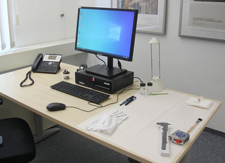 Foto eines Schreibtisches, auf dem prominent ein Computerbildschirm und eine Tastatur platziert sind