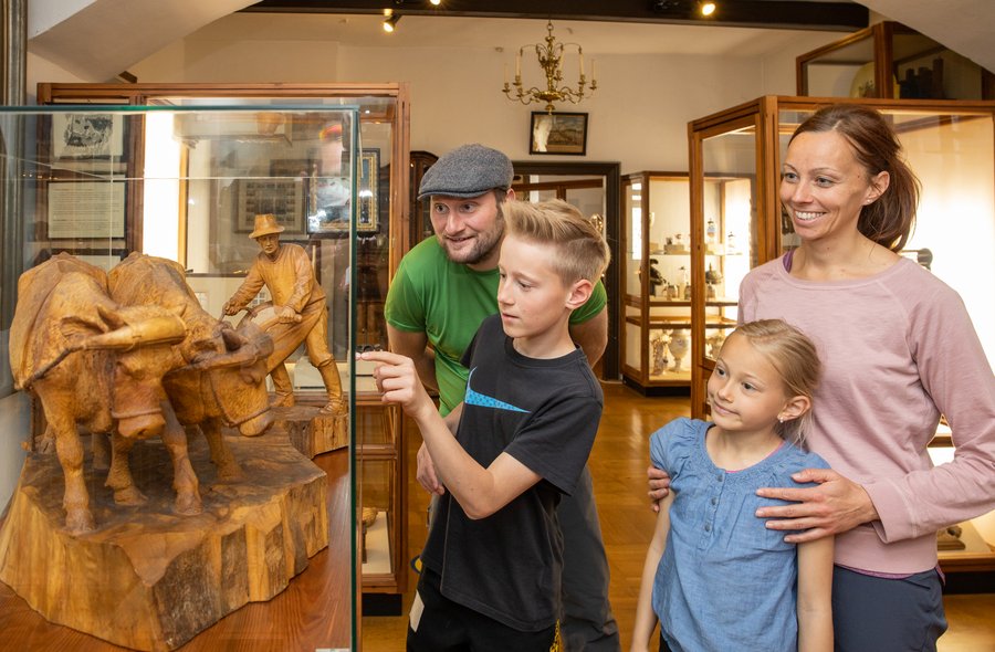 In einem Ausstellungsraum betrachten zwei Kinder mit ihren Eltern ein großes Holzschnitzwerk in einer Vitrine.