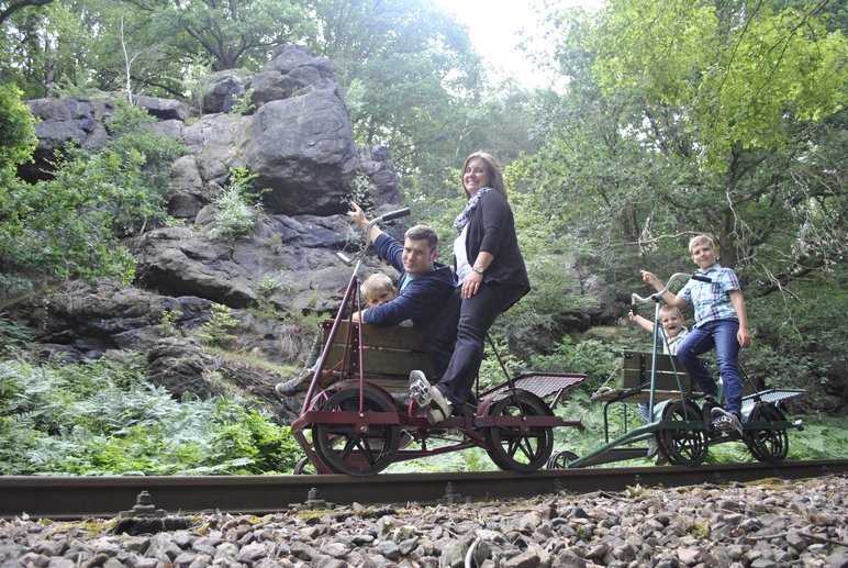 Zwei Erwachsene und drei Kinder fahren auf zwei Fahrrad-Draisinen durch eine felsige Landschaft.