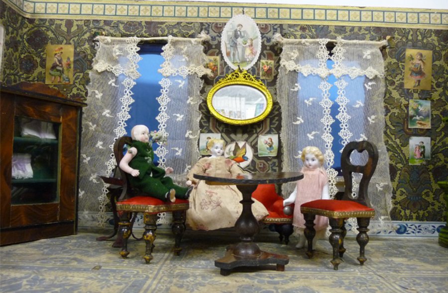 Miniaturversion der Stube einer wohlsituierten Familie, in der Vater, Mutter und Kind sitzen