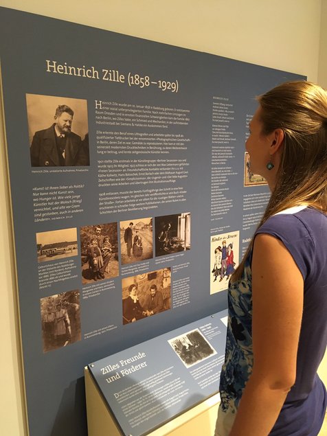 Eine Frau steht lesend vor dem mit Fotos bebilderten Wandtext zu Heinrich Zille.