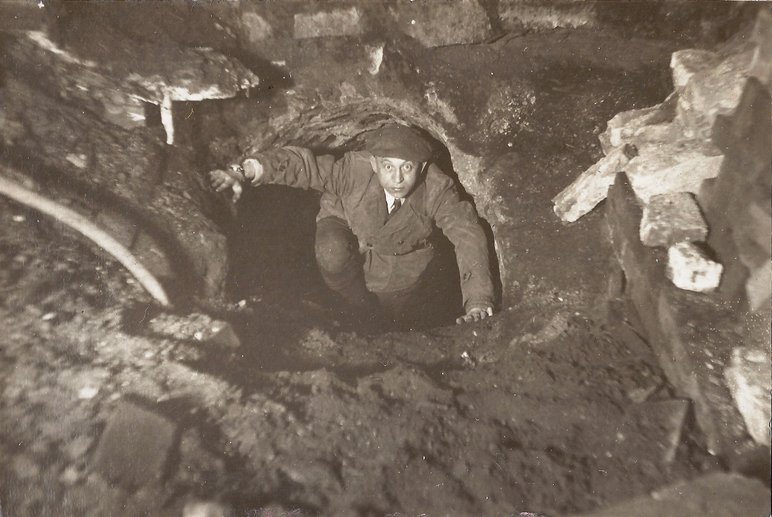 Das Schwarzweiß-Foto blickt von oben auf einen Mann, der durch einen unterirdischen Gang nach oben steigt und direkt in die Kamera blickt.