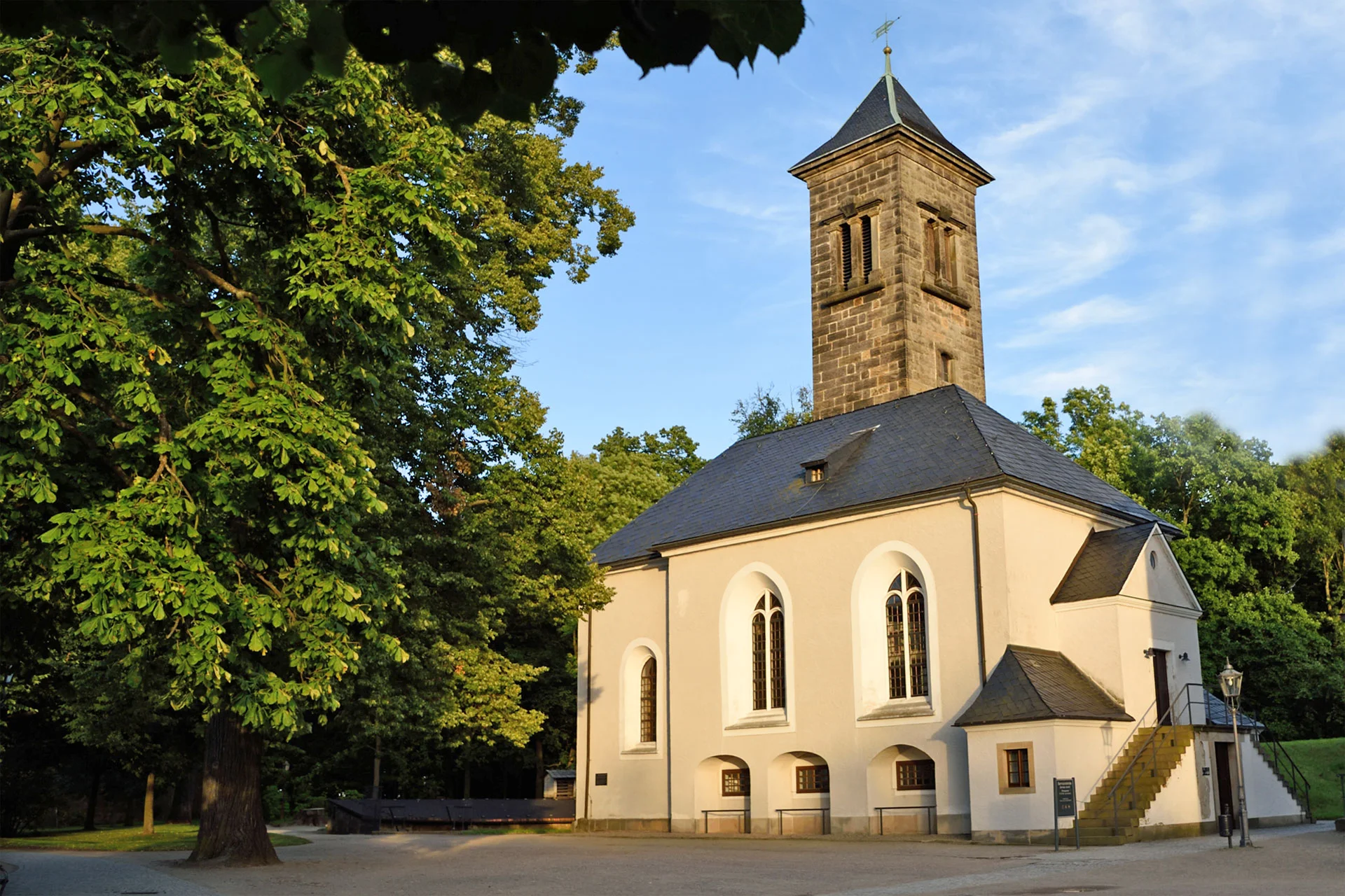 Westansicht der Garnisonskirche auf der Festung Königstein in warmem Abendlicht, umgeben von dicht belaubten Bäumen