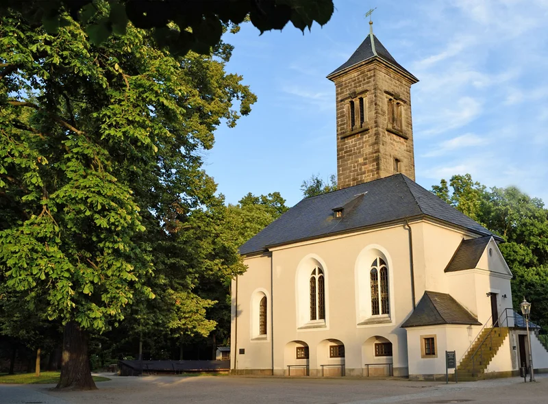 Westansicht der Garnisonskirche auf der Festung Königstein in warmem Abendlicht, umgeben von dicht belaubten Bäumen