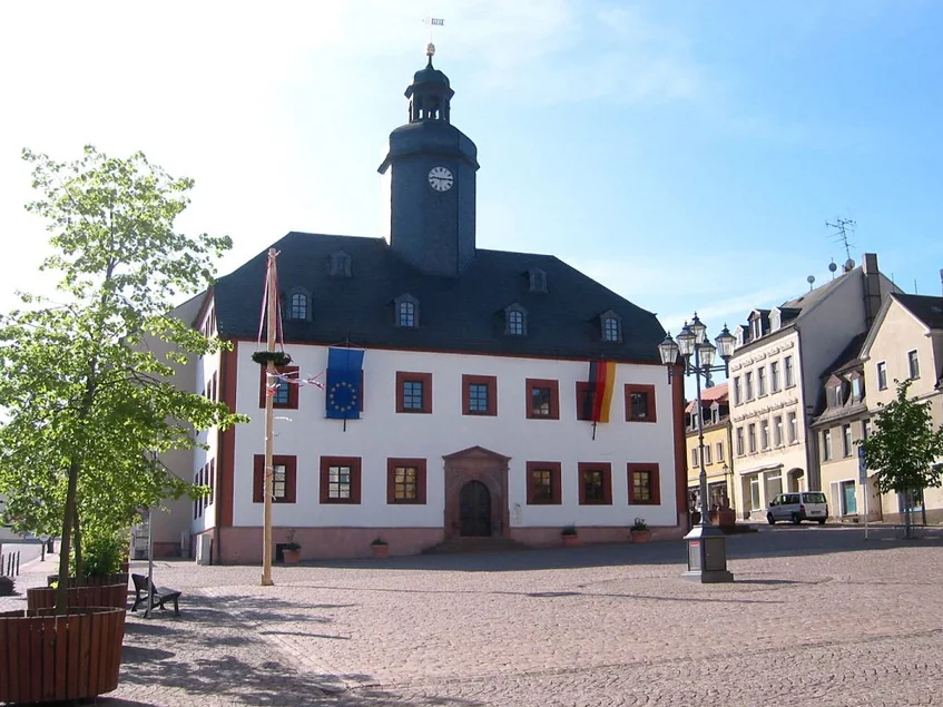 Das Alte Rathaus beherbergt das Museum Meerane. Sommerliche Außenansichtes eines dreistöckigen weißen Gebäudes mit schwarzem Schieferdach und einem zentral angeordneten schwarzen Türmchen, das am Rande eines großen, Kopfstein-gepflasterten Platzes steht