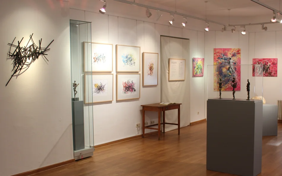 Ausstellungsraum mit kleinen Bronzefiguren sowie farbenfrohen abstrakten Zeichnungen und Gemälden