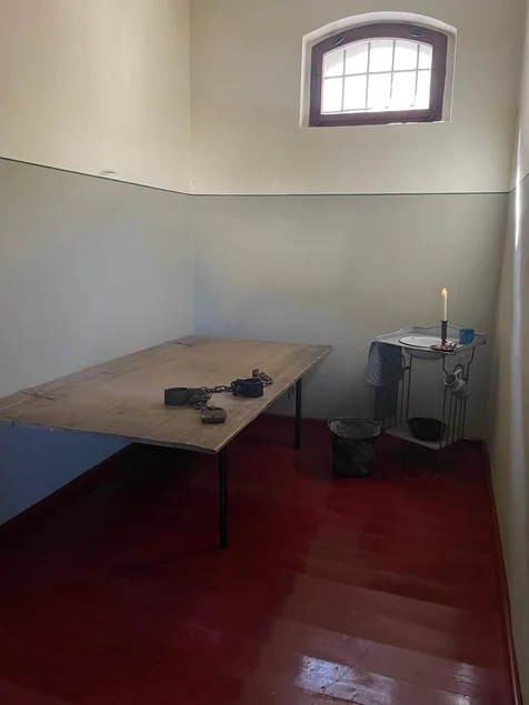 Eine ehemalige Gefängniszelle mit verschiedenen Gegenständen wird von einem Trunkenbold besprochen.