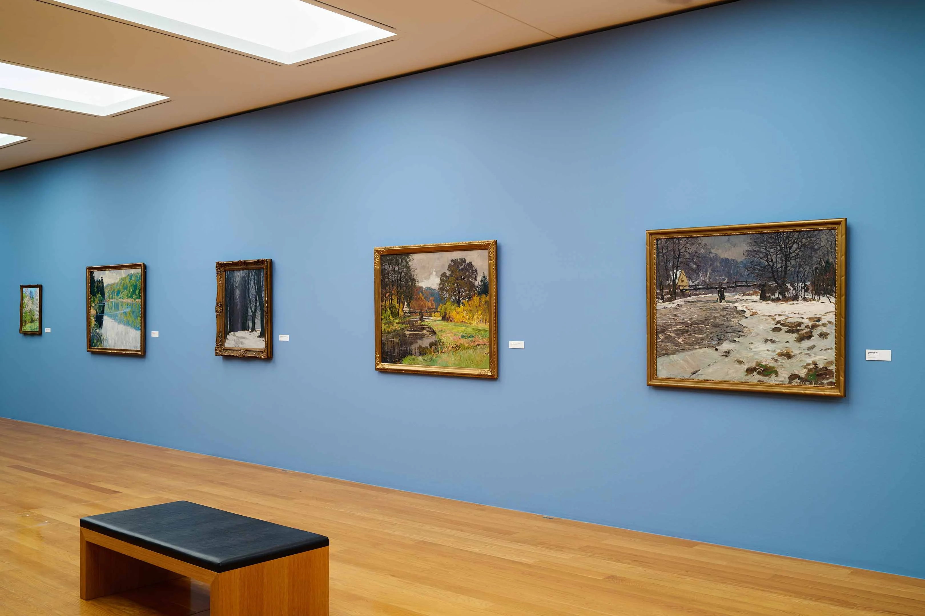 Fünf impressionistisch anmutende Landschaftsgemälde hängen an hellblauer Wand.