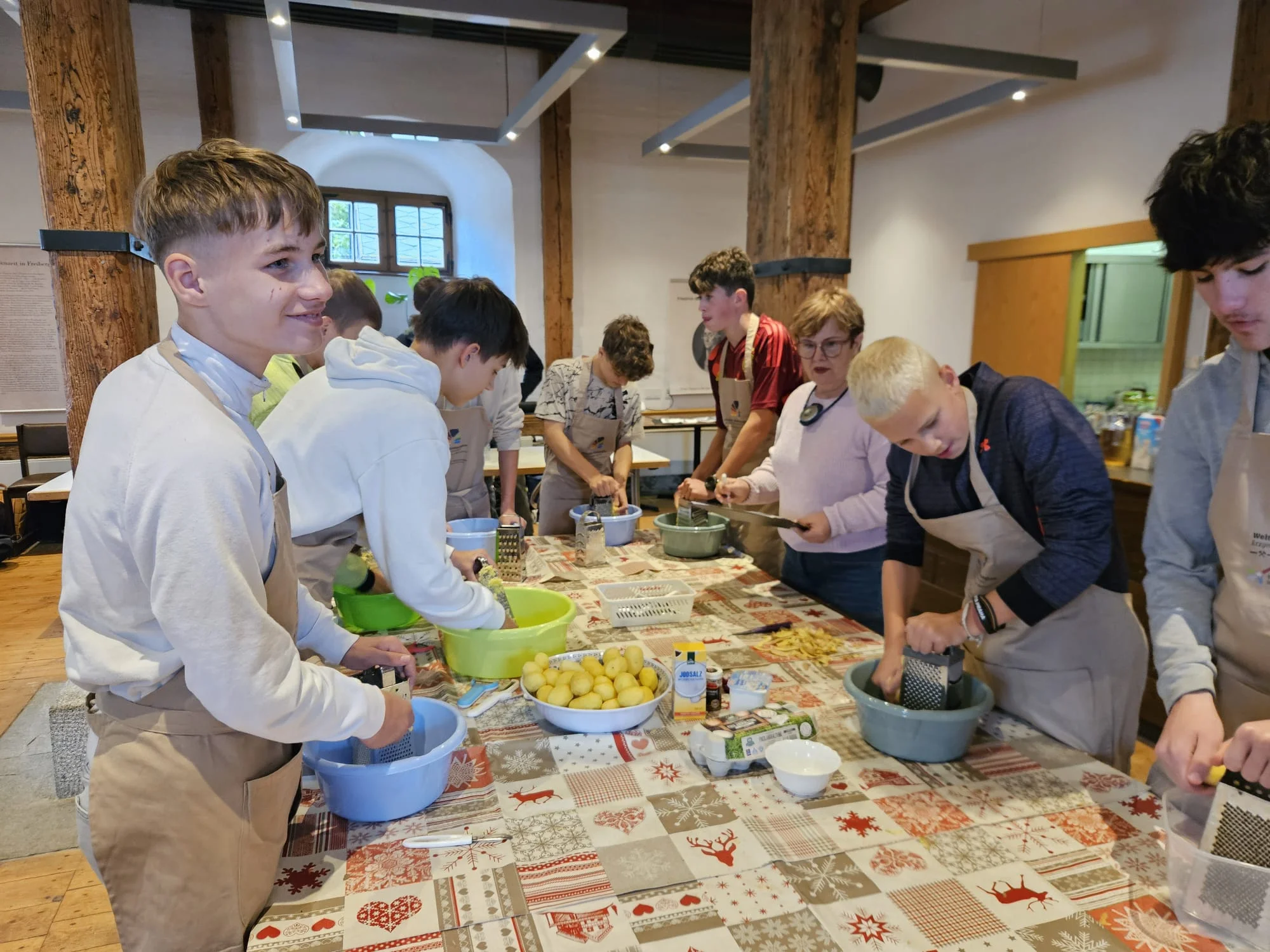 Küchenwerkstatt Gemeinsames Kartoffelreiben an einem langen Tisch; Teilnehmende mit Schürzen arbeiten konzentriert.