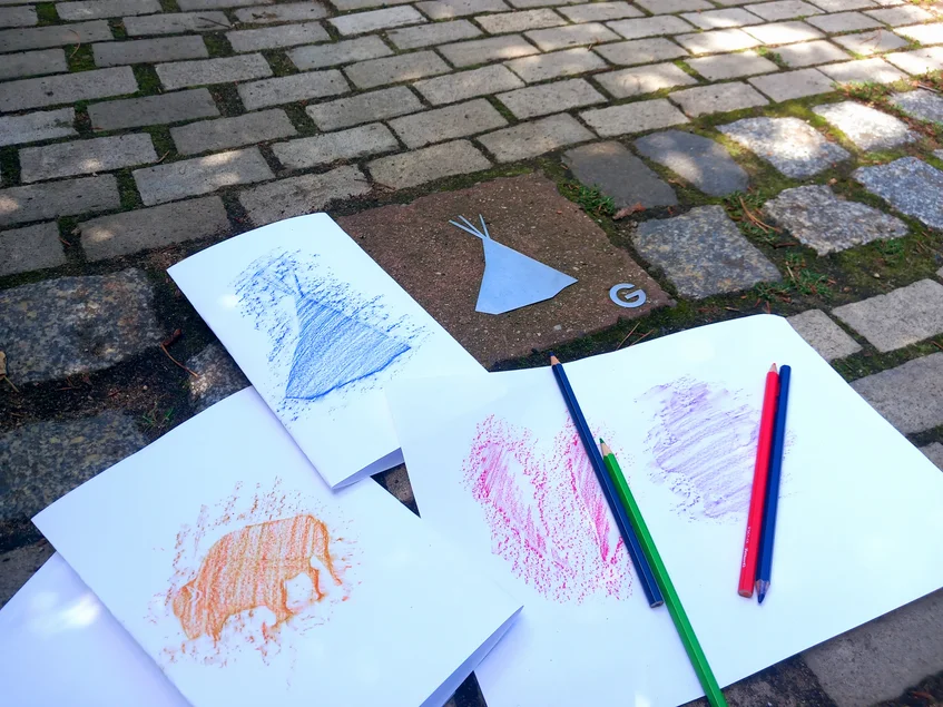 Ein Spurenstein auf dem Weg ins Museum, der ein Tipi zeigt. Daneben liegen bunte Schraffuren von verschiedenen Spurensteinen.