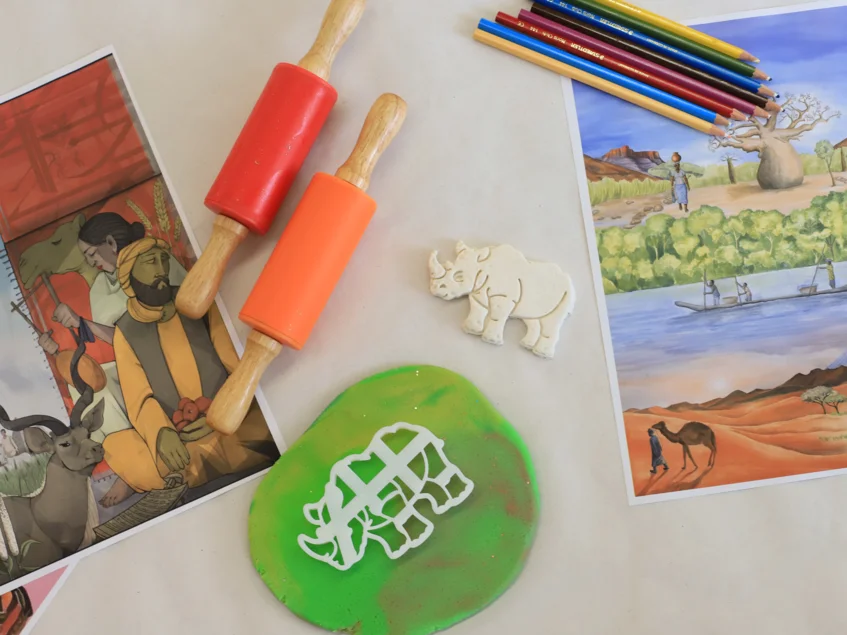 Atelier Africa Auf einer Tischplatte liegen verschiedene Bastelmaterialien: Teigrollen, ausgerollte Knete, Buntstifte, eine Nashorn-Ausstechform sowie ein ausgestochenes Nashorn.