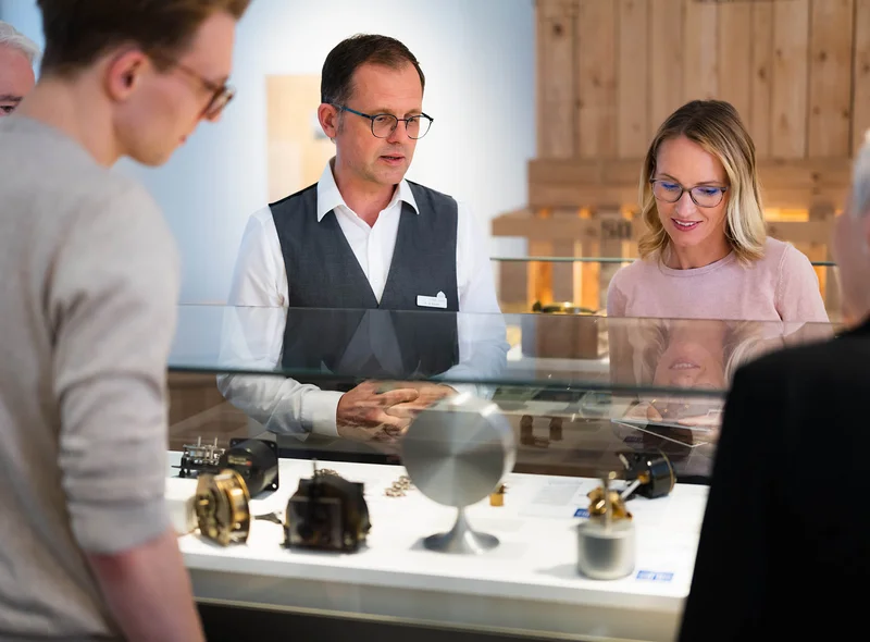 Museumsmitarbeiter erklärt kleiner Gruppe Objekte in einer Vitrine.