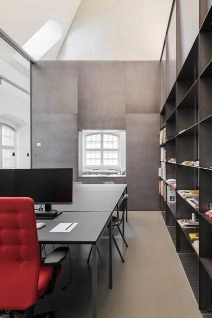 In der Mitte des Raumes befindet sich ein großer Tisch mit einem Computer. An den Wänden sind Regale angebracht.