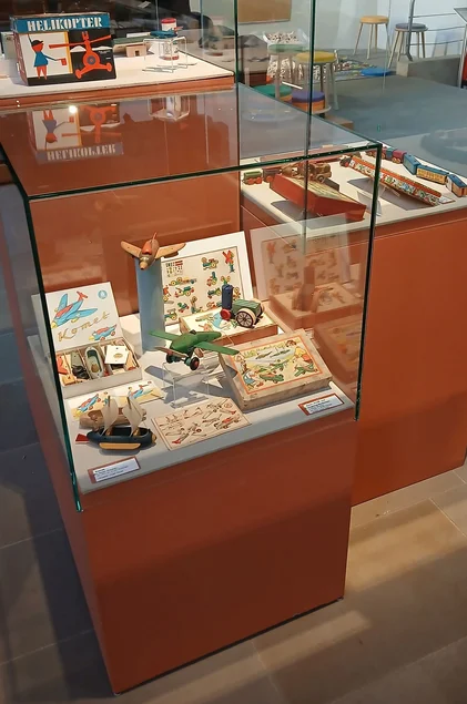 In einer Sockelvitrine sind verschiedene Spielfahrzeuge mit ihren Verpackungen und Bauanleitungen ausgestellt.