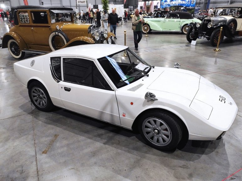 Auf einer Ausstellungsfläche stehen mehrere historische Automobile, im Vordergrund ein weißer, aerodynamisch geformter Rennwagen.