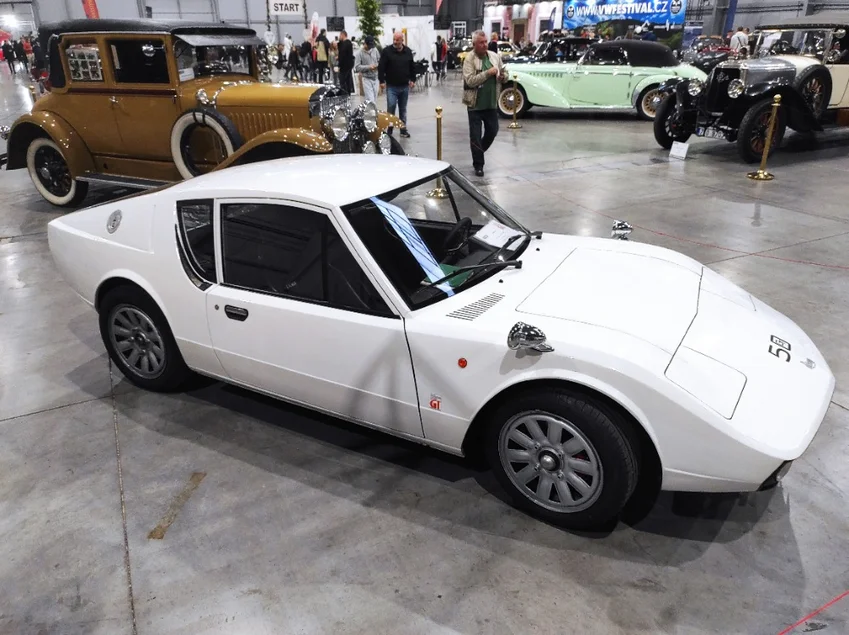 Experiment des Forschungsinstituts für Kraftwagen Auf einer Ausstellungsfläche stehen mehrere historische Automobile, im Vordergrund ein weißer, aerodynamisch geformter Rennwagen.