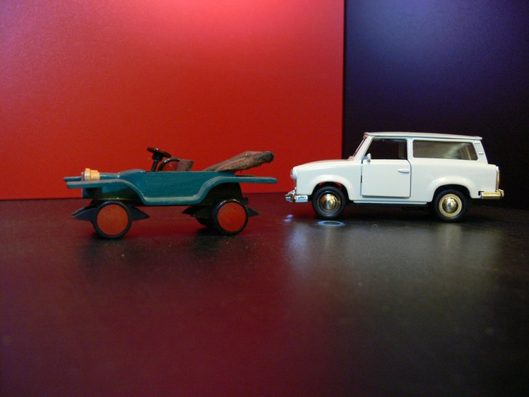 Zwei historische Fahrzeugmodelle stehen vor einer Wand in Rot und Blau.