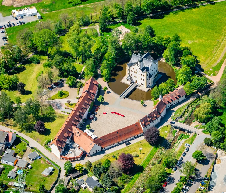 Schlossensemble Klaffenbach Luftbildaufnahme eines kleinen, weiß getünchten, von einem Wassergraben umgebenen Renaissance-Schlosses, an das sich V-förmig ein rot gedecktes Schloss-Vorwerk anschließt. Das Ensemble ist umgeben von Grünflächen.