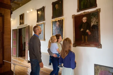 Ferienprogramm „Kindsköpfe“ im Schloss Museum Glauchau Eine Familie betrachtet goldgerahmte Gemälde an der Wand. Auf einem Bild ist ein Kind in historischer Kleidung zu erkennen.