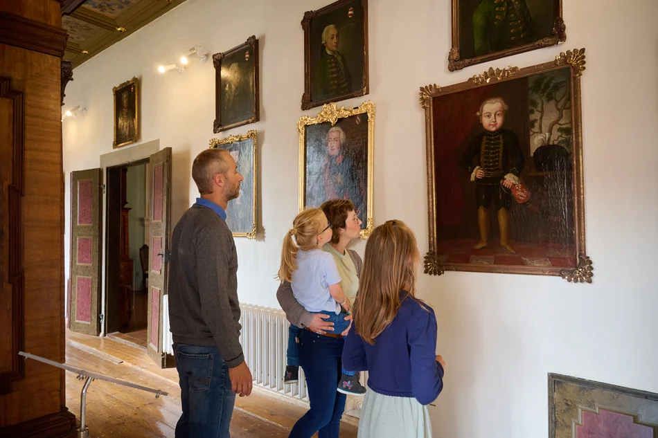 Ferienprogramm „Kindsköpfe“ im Schloss Museum Glauchau Eine Familie betrachtet goldgerahmte Gemälde an der Wand. Auf einem Bild ist ein Kind in historischer Kleidung zu erkennen.