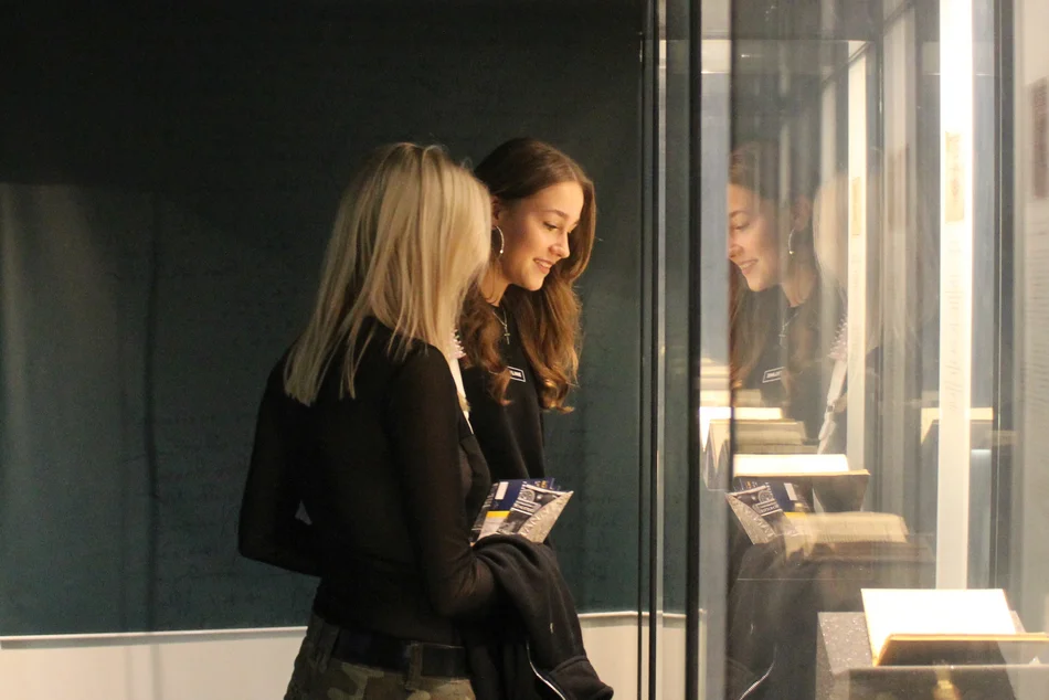 Zwei Frauen schauen in eine große beleuchtete Vitrine, in der ein aufgeschlagenes Buch ausgestellt ist.