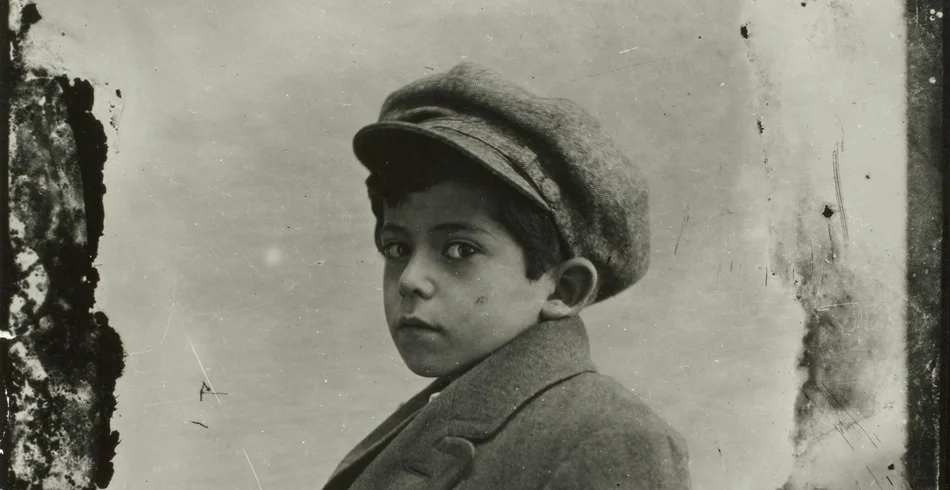 Historisches Porträtfoto eines Jungen mit Hut, der direkt in die Kamera schaut. Das Foto ist in Schwarzweiß.