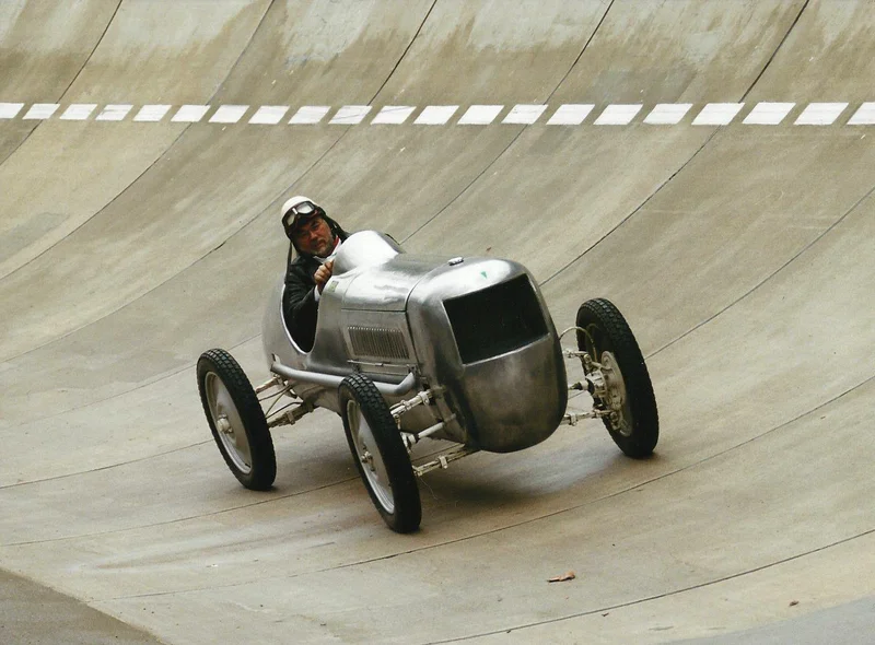 Ein Mann fährt auf einer Rennstrecke einen historischen Rennwagen mit relativ kleiner Metallkarosse und relativ großen Rädern
