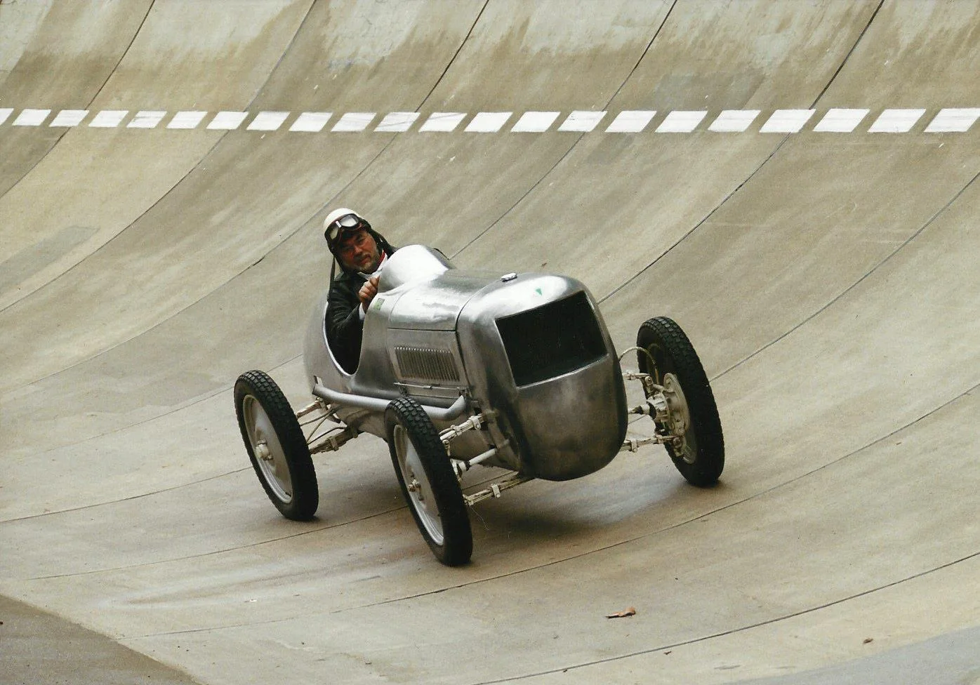 Frieder Bach im Fachsenfeld-Rennwagen Ein Mann fährt auf einer Rennstrecke einen historischen Rennwagen mit relativ kleiner Metallkarosse und relativ großen Rädern