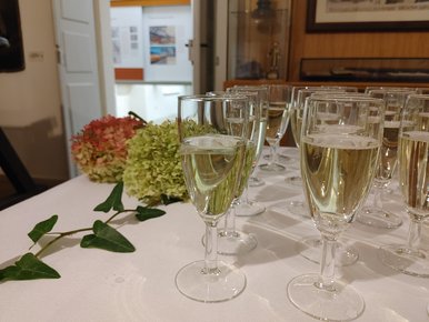 Veranstaltungsreihe „MUSecco“ Das Foto zeigt einige Gläser Prosecco und zwei Blumen auf einem Tisch mit weißer Tischdecke.