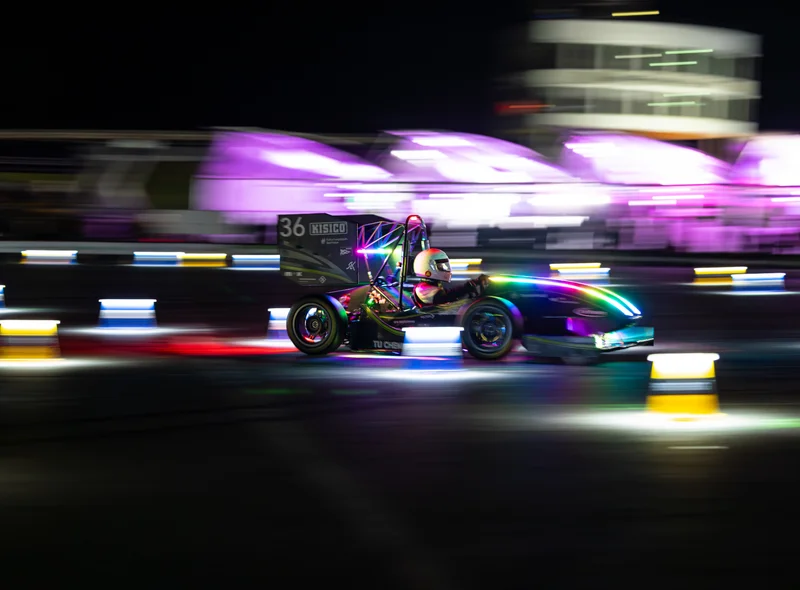 Ein Rennwagen fährt im Dunkeln mit hoher Geschwindigkeit vorbei an bunten, verschwommenen Lichtern.