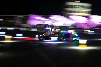 Ein Rennwagen fährt im Dunkeln mit hoher Geschwindigkeit vorbei an bunten, verschwommenen Lichtern.