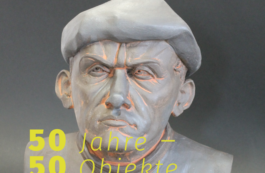 Auf dem Foto einer geschnitzten Büste eines Mannes mit Baskenmütze steht in Gelb der Schriftzug Jubiläumsausstellung „50 Jahre – 50 Objekte“.