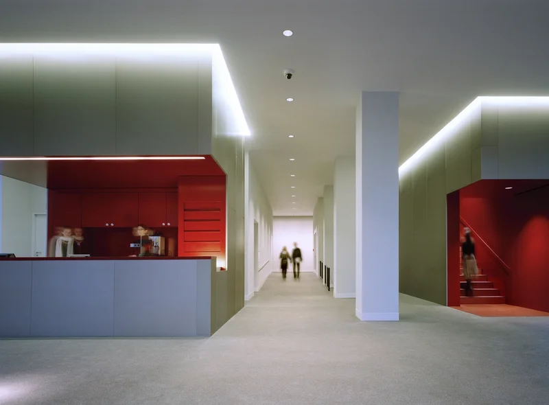 Das Foto zeigt das in Weiß gehaltene Foyer des Museum Gunzenhauser. Links und rechts öffnen bodentiefe Panoramafenster die Sicht nach außen. Innen, auf der linken Seite, befindet sich die Kasse; mittig schließt sich ein langer Gang zu den Ausstellungsräumen im Erdgeschoss an. Rechts des Ganges befindet sich das schmale, steile Treppenhaus, das in die Ausstellungräume in den Obergeschossen führt. Kasse und Treppenhaus sind in einem tiefen Rot gehalten.