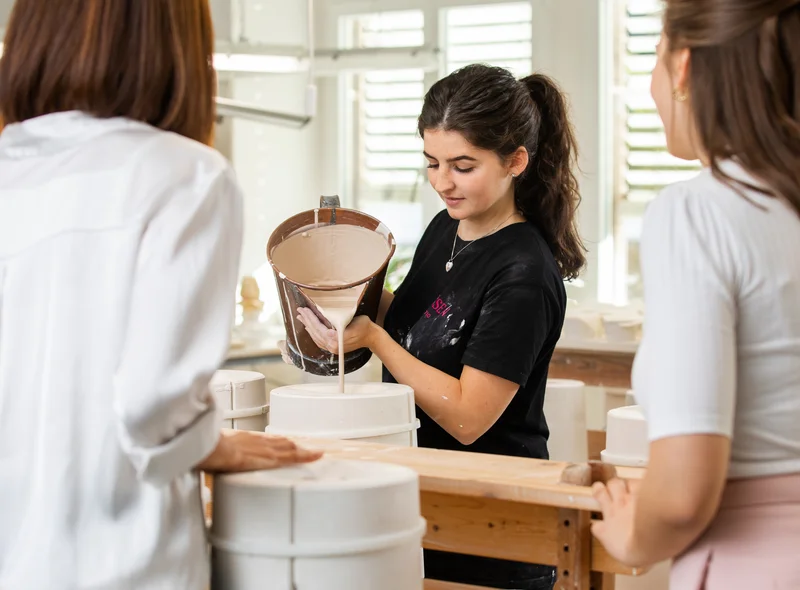 Im Workshop "Gießen" füllt eine Mitarbeiterin flüssige Porzellanmasse in eine Form – ein anschaulicher Einblick ins Handwerk.