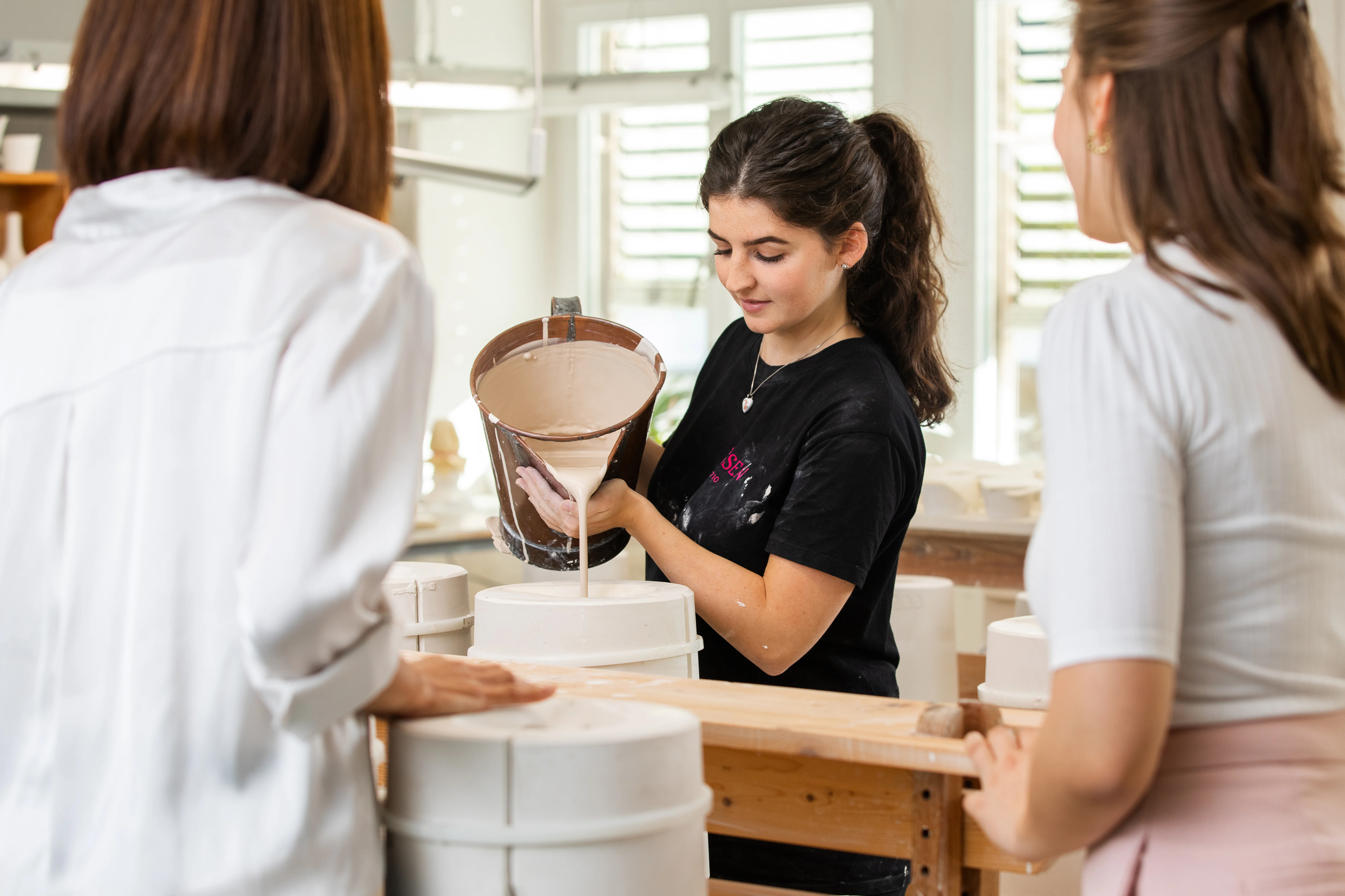 Im Workshop "Gießen" füllt eine Mitarbeiterin flüssige Porzellanmasse in eine Form – ein anschaulicher Einblick ins Handwerk.