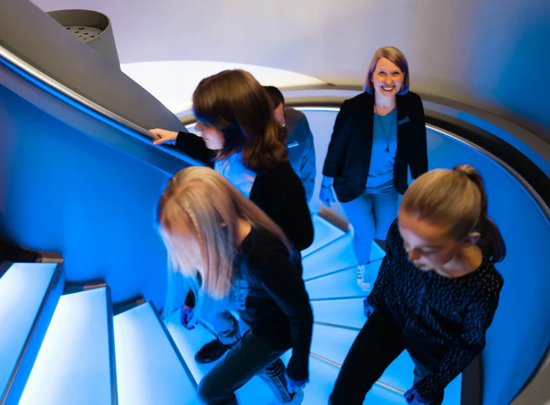Kindergruppe erklimmt die blau beleuchtete Wendeltreppe, genannt Zeittreppe, ins Museum