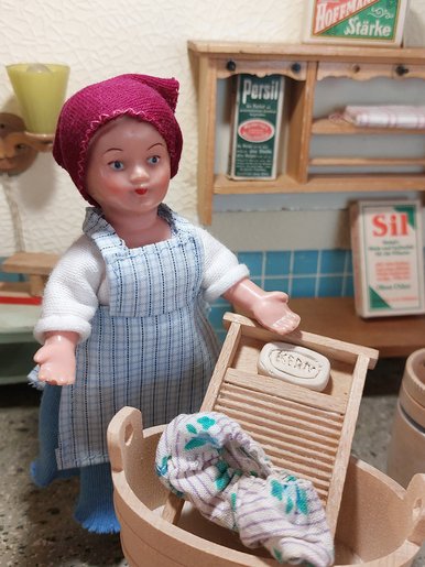 Puppenstube mit einer Waschküche Eine Puppe an einer Miniatur-Waschmaschine