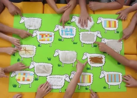 Auf grünem Untergrund sind gewebte Papier-Schafe aufgebracht.