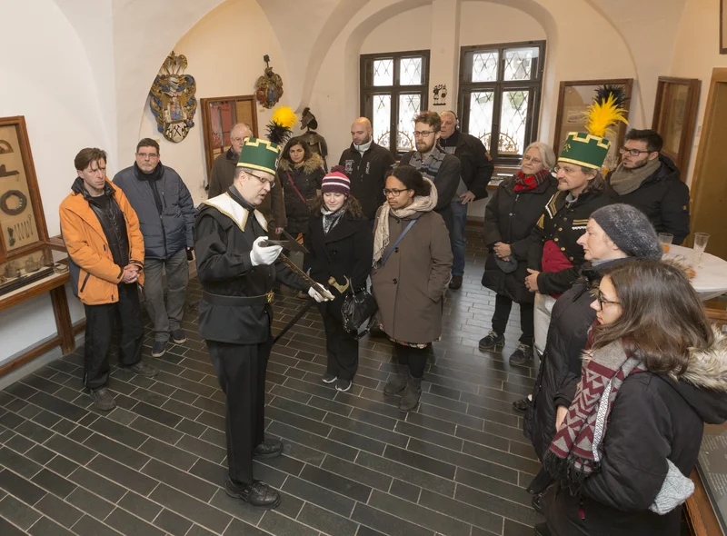 Ein Mann in traditioneller erzgebirgischer Bergmanns-Uniform zeigt Gästen im Erzgebirgsmuseum historisches Bergbau-Werkzeug.