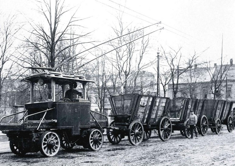 Historisches Schwarzweißfoto einer nicht auf Gleisen fahrenden Bahn mit drei offenen Gütertransportwagen