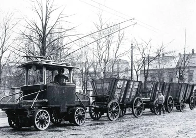 Historisches Schwarzweißfoto einer nicht auf Gleisen fahrenden Bahn mit drei offenen Gütertransportwagen