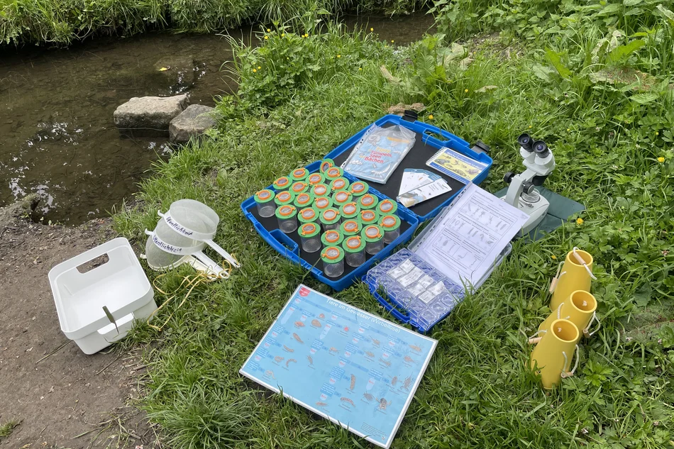 Materialien für Gewässeruntersuchung sind am Ufer eines Baches ausgebreitet.