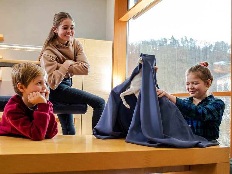 Das Foto zeigt drei Kinder und eine unter einer Decke verborgene Porzellanfigur