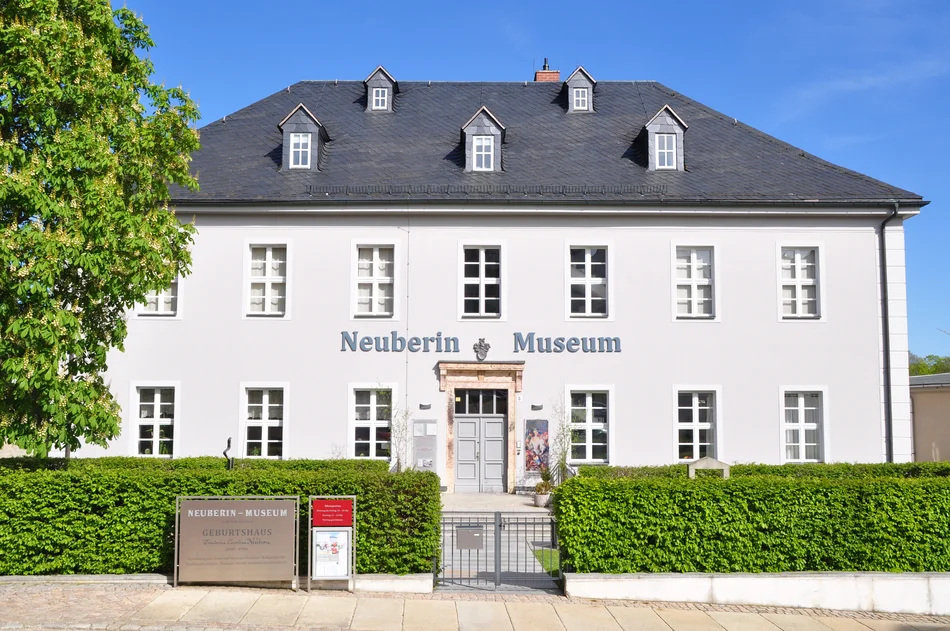 Zweistöckiges Gebäude mit dem Schriftzug "Neuberin Museum", weißer Fassade und einem schiefergedeckten Dach mit Gauben