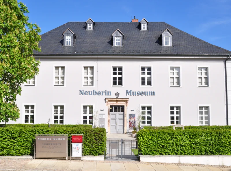 Zweistöckiges Gebäude mit dem Schriftzug "Neuberin Museum", weißer Fassade und einem schiefergedeckten Dach mit Gauben