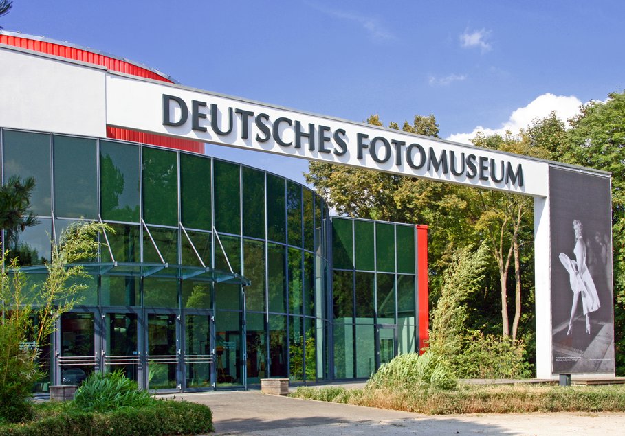 Ein moderner Rundbau mit Glasfassade, darüber der Schriftzug "Deutsches Fotomuseum" und daneben die banner-artige Reproduktion eines historischen Schwarzweißfotos