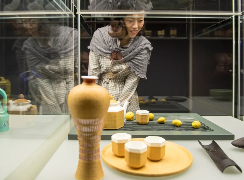 Eine Frau mit Schultertuch betrachtet gelb glasierte Keramik, die in einer Vitrine präsentiert wird.