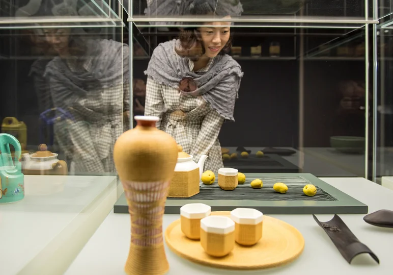 Eine Frau mit Schultertuch betrachtet gelb glasierte Keramik, die in einer Vitrine präsentiert wird.