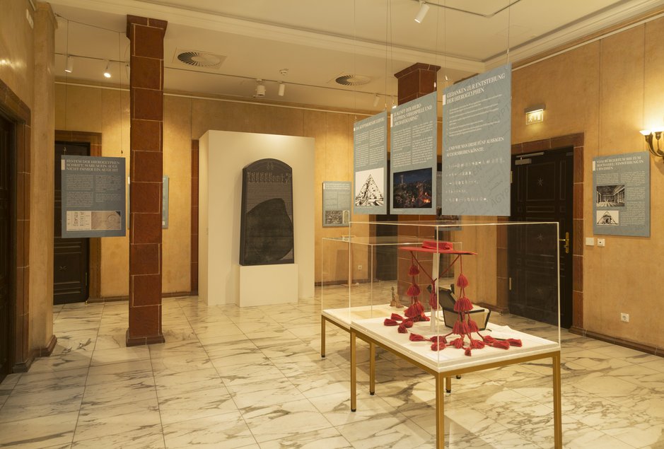 Das Foto zeigt eine Ausstellungsfläche mit Vitrinen, im Hintergrund eine Rekonstruktion des Rosettasteins.
